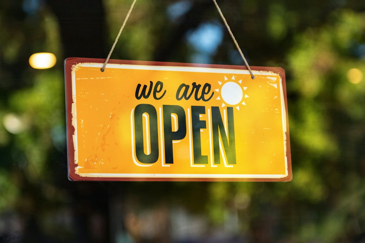 Yellow We Are Open sign hanging in a shop doorway